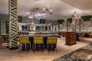 Zona de bar moderna con barra central, varias opciones de asientos y un llamativo diseño de pared geométrico.