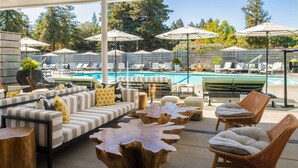 Un espace de détente aménagé au bord de la piscine, avec des canapés à rayures, des tables rondes en bois, des fauteuils en osier et des parasols.