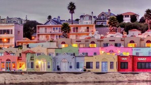 A waterfront property with colorful buildings, a sandy beach, and a calm body of water reflecting the structures. - Iconic Nature Views | Monterey Bay. Pool (Santa Cruz)