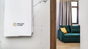 Une chambre d’hôtel avec un mur en marbre, un canapé vert et une fenêtre avec des rideaux.