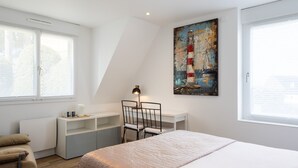 Ett sovrum med en säng, ett skrivbord, en stol och en målning av ett fyrtorn.