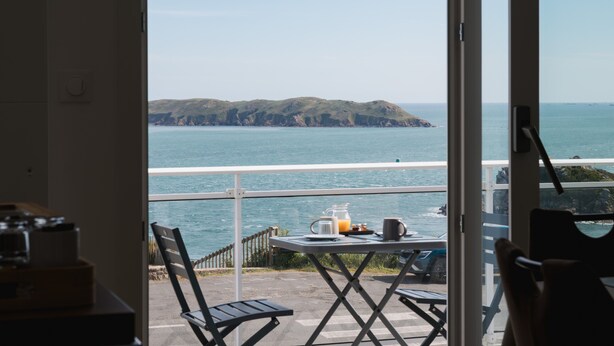 Ein Balkon mit gedecktem Frühstückstisch, mit Blick auf die Küste und eine kleine Insel.