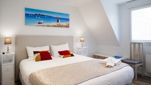 Ein Schlafzimmer mit einem großen Bett, zwei Nachttischen, einem Beistelltisch, einem Sessel, einem Bild an der Wand und einem Fenster.