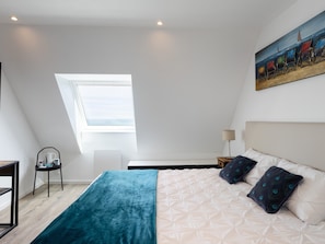 A bedroom with a bed, a skylight, a painting, and a chair.