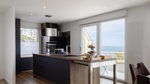 Une cuisine moderne dotée d’un grand îlot central, d’appareils électroménagers intégrés et offrant une vue sur la mer.