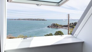 Une fenêtre de toit offrant une vue sur la mer et le paysage lointain.