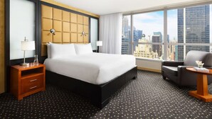 Habitación de hotel con una cama grande, una mesita de noche, una silla y vistas a la ciudad.