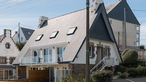 Une maison moderne avec un toit en pente, un balcon et un mur en pierre à l’avant.