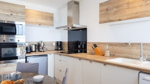Une cuisine moderne dotée d’un plan de travail en bois, d’appareils électroménagers en acier inoxydable et d’un coin repas avec une table dressée pour deux personnes.
