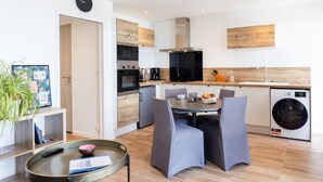 Une cuisine moderne dotée d’appareils électroménagers intégrés, un coin repas avec des chaises grises et un lave-linge.