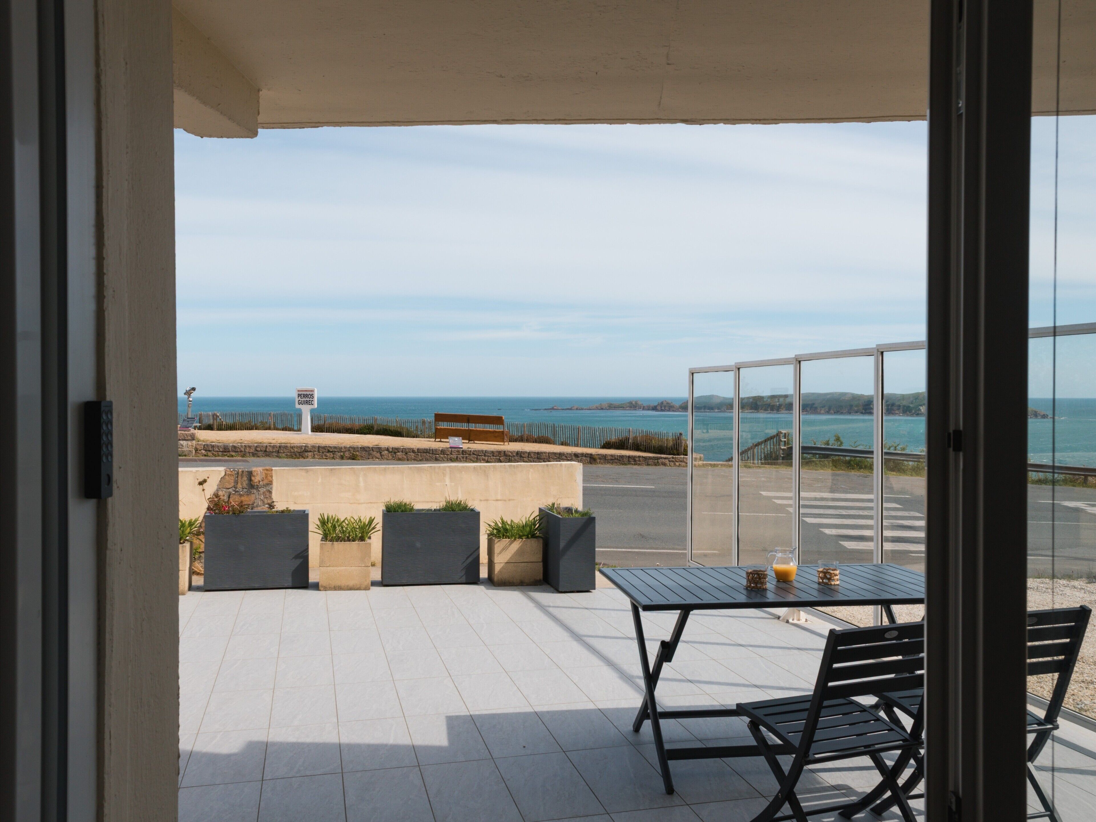 A balcony with a view of the sea, a table with chairs, and potted plants.