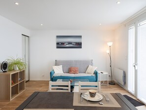 Un salon moderne avec un canapé, une table basse, une lampe sur pied, une bibliothèque et un tableau accroché au mur.