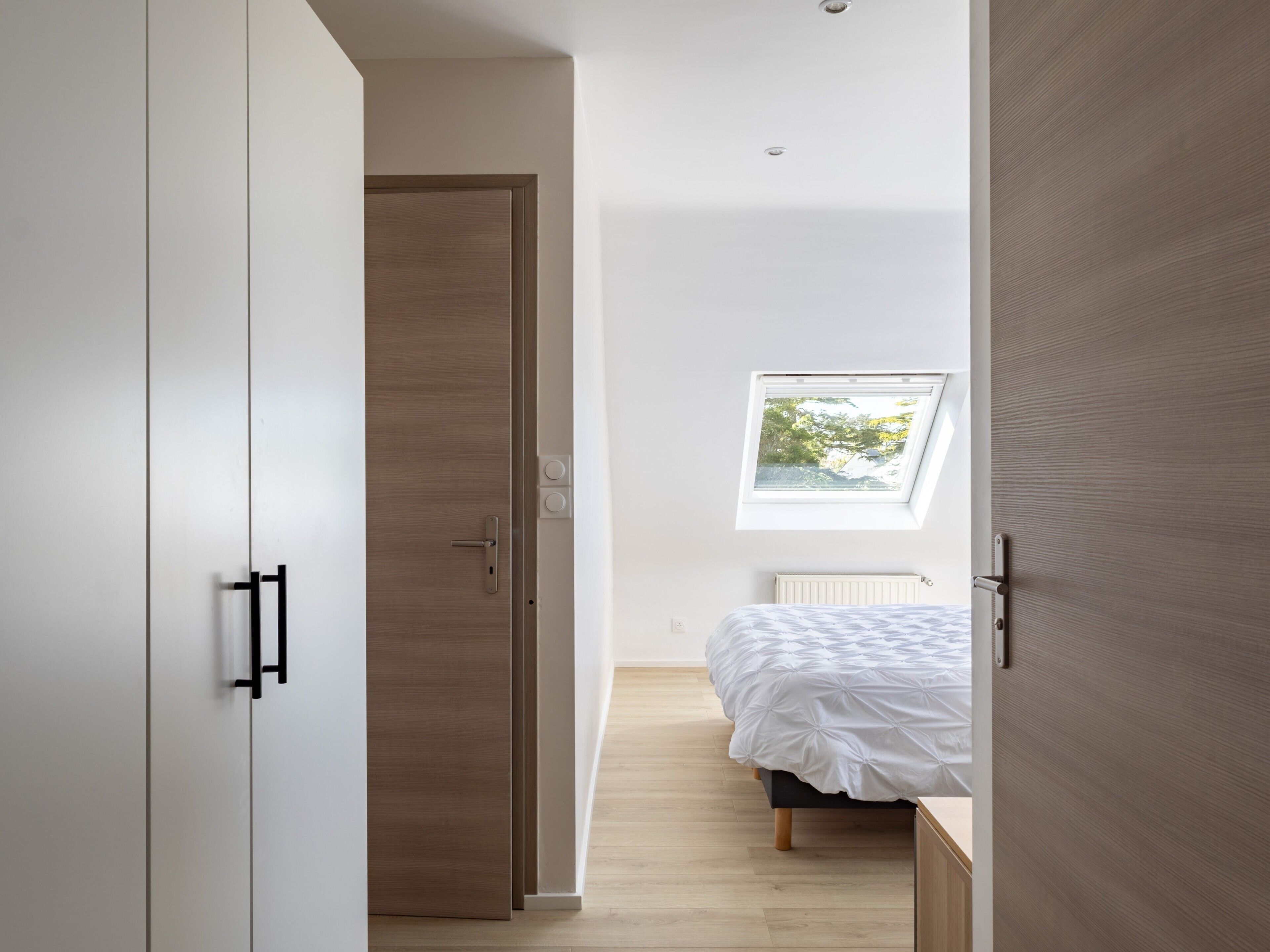 Een slaapkamer met dakraam, een bed, een kledingkast en een radiator.
