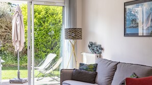 Ein modernes Wohnzimmer mit einer Couch, einem Glastisch, einer Lampe und Blick auf einen Garten durch eine Glasschiebetür.