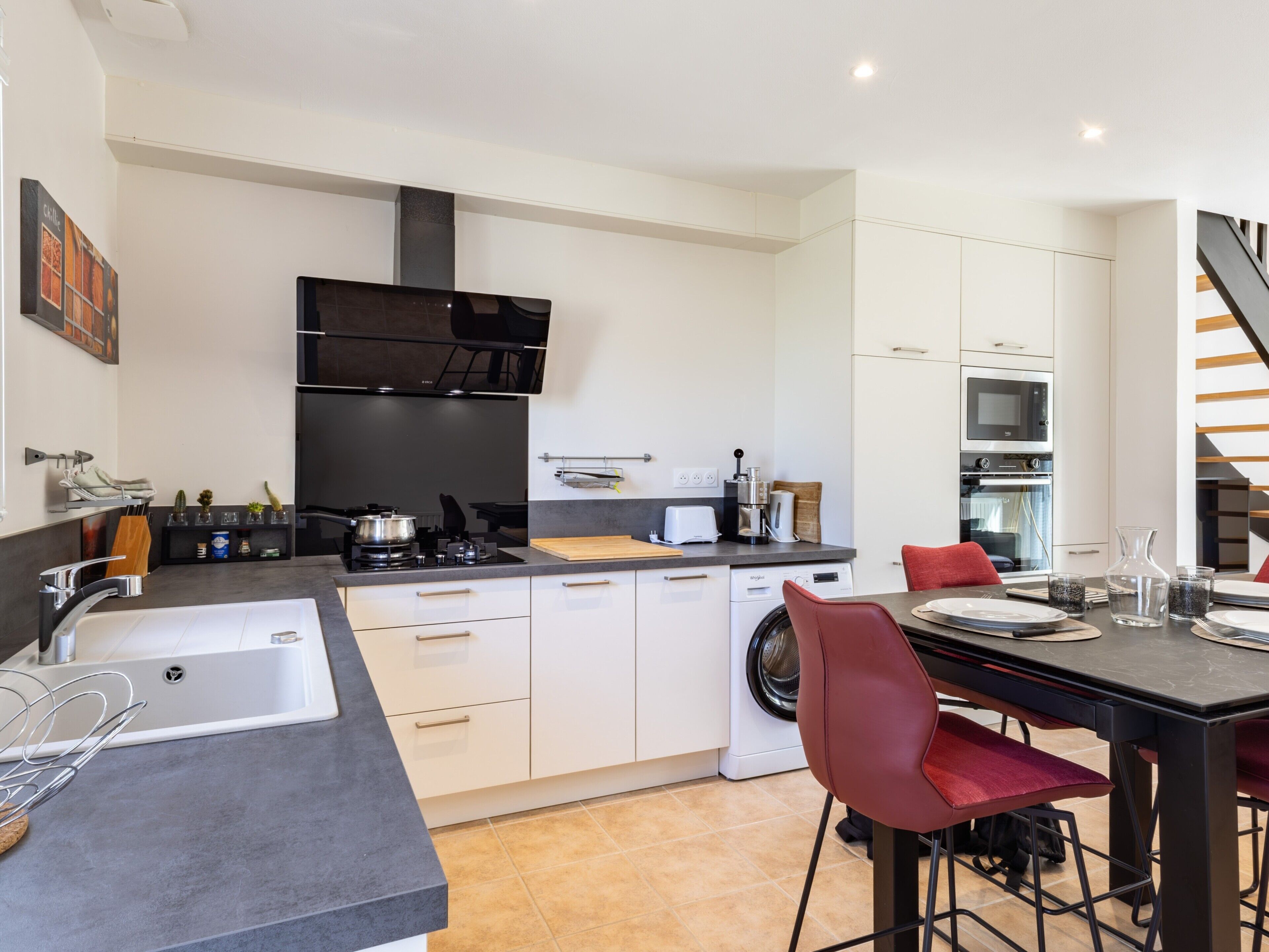 A modern kitchen with a stove, sink, and dining area with chairs.
