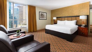 A hotel room with a bed, a desk, a chair, a window with curtains, and a city view.