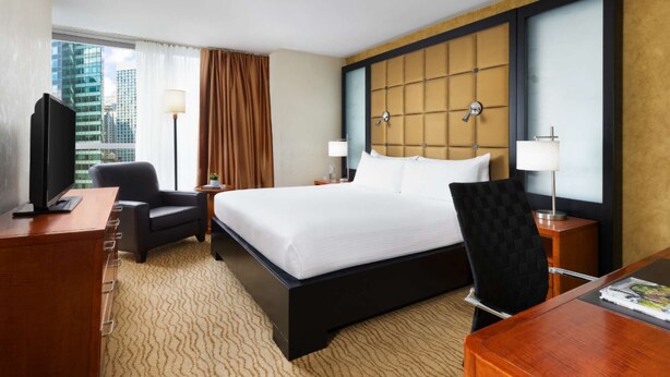 A hotel room with a large bed, a desk, a chair, a TV, and a window with curtains.