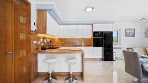 Eine moderne Küche mit weißen Schränken, einer Holzauskładung, zwei weißen Barhocker und einem schwarzen Kühlschrank.
