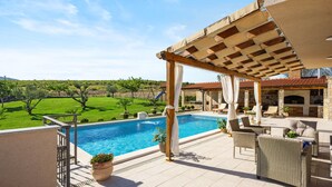 Ein Poolbereich mit einer Pergola, Liegestühlen und einem Kamin aus Stein.