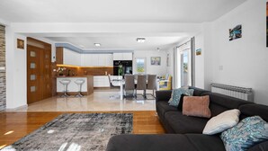 Ein modernes Wohnzimmer mit einem dunklen Sofa, einem gemusterten Teppich und einem Essbereich mit Stühlen und einem Tisch.