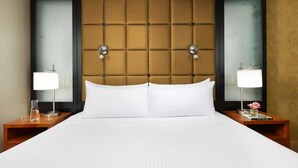Una habitación de hotel con una cama grande, dos mesitas de noche con lámparas y un cabecero capitonado.