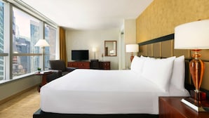 Habitación de hotel con una cama grande, televisión, escritorio y vistas a la ciudad.