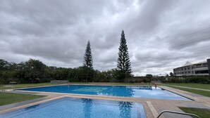 Une piscine rectangulaire dont le bord est recouvert de carreaux, entourée d’une pelouse et d’arbres.