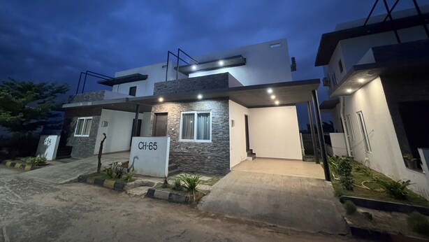Une maison moderne à deux étages, dotée d’une façade en pierre, portant le numéro CH-65, et dont l’entrée est bien éclairée.