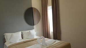 Un lit bien fait, aux couleurs beige et blanc, avec un ventilateur de plafond et un appareil de climatisation fixé au mur.