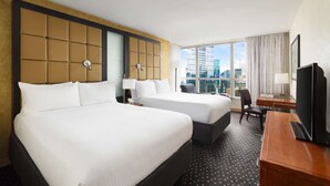 A hotel room with two beds, a desk, a chair, a TV, and a large window with a city view. - Premier Paradise | Rockefeller l Ball Drop view (New York)