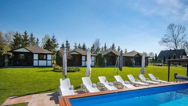 A swimming pool with lounge chairs, a wooden deck, and a row of cabins in the background. - Comfortable Holiday Homes, Jacuzzi, Summer Pool (Postomino)
