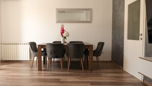 Ein Essbereich mit einem Holztisch, vier Stühlen, einer Blumenvase, einem Heizkörper und einer Tür mit satiniertem Glas.