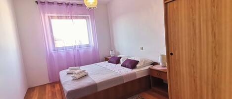A bedroom with a bed, bedside lamps, a wooden wardrobe, and a window with curtains.