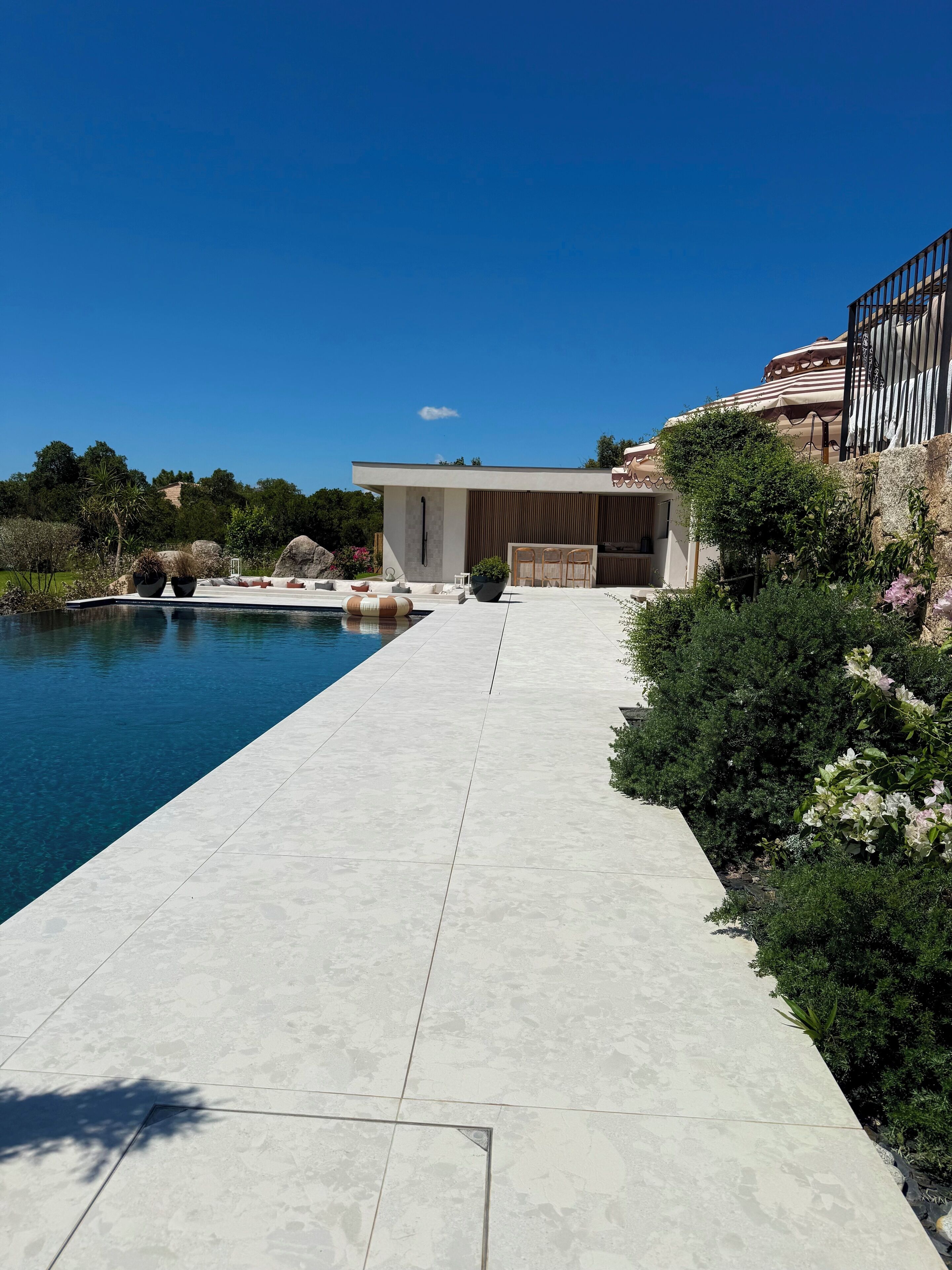 Un espace piscine moderne avec une piscine à l’eau d’un bleu limpide, une allée dallée et un bâtiment doté d’un patio couvert.