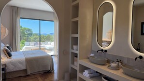 Ett modernt hotellrum med en stor säng, ett badrum med dubbelt handfat och en balkong med utsikt över bergen.