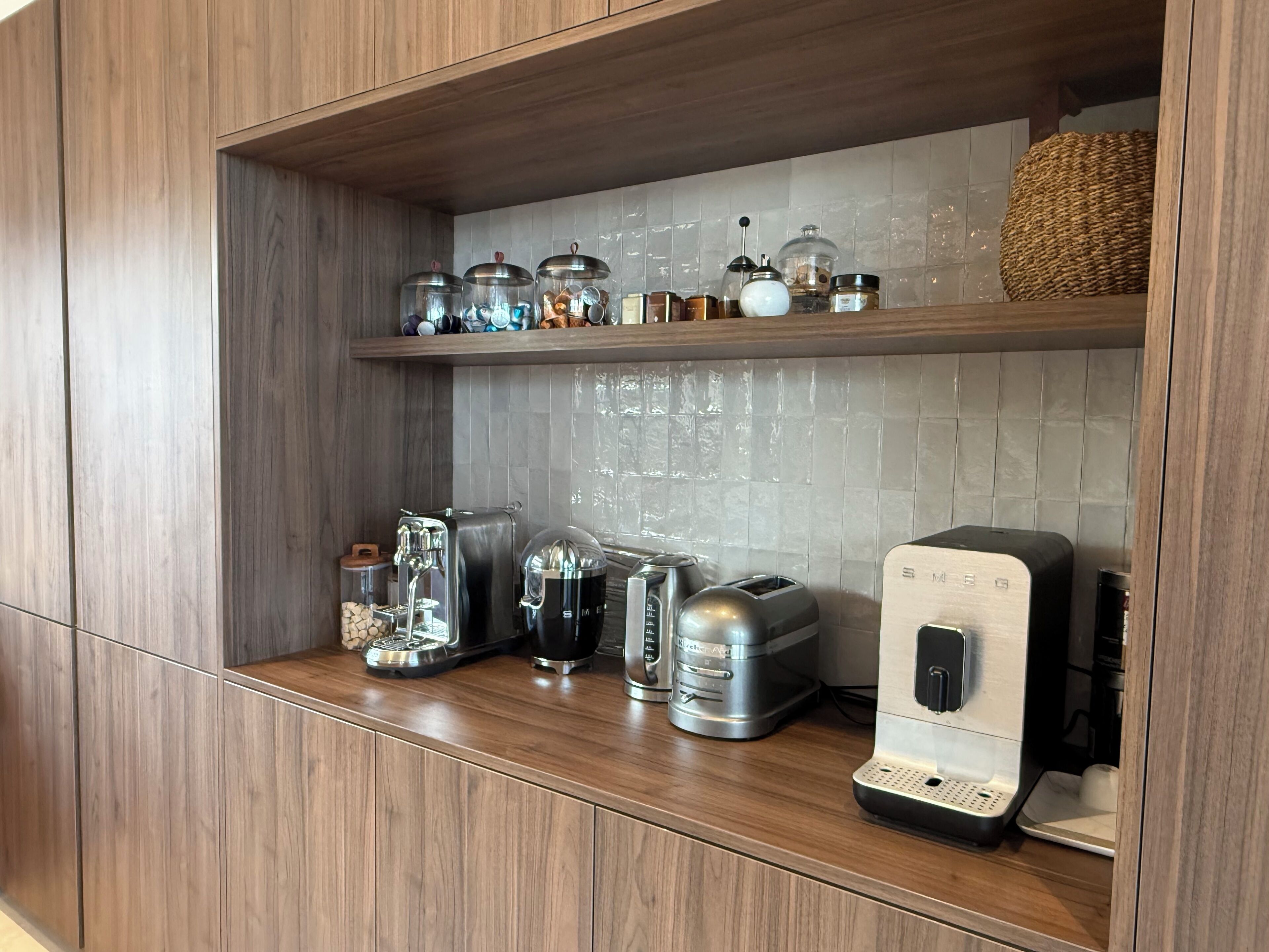 Una cocina con armarios de madera, una cafetera de acero inoxidable, un tostador y varios frascos en una estantería.
