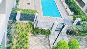 Ein Poolbereich auf dem Dach mit einem rechteckigen Pool, umgeben von Grünflächen und modernen Gebäuden.