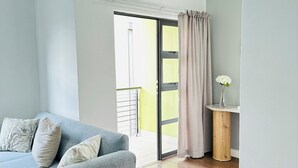 Ein modernes Wohnzimmer mit grauem Sofa, Holzboden und einer Schiebeglastür, die auf einen Balkon führt.