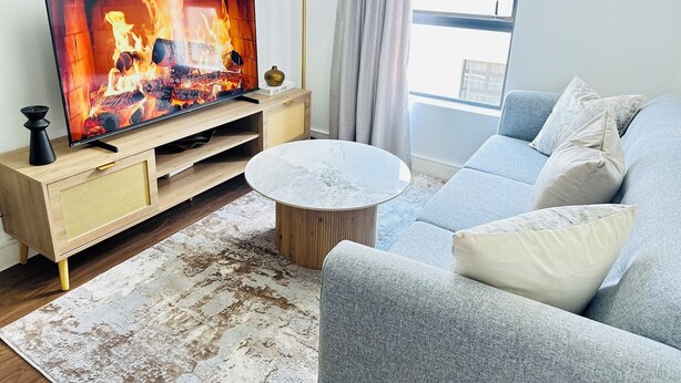 Ein Wohnzimmer mit Flachbildfernseher, der einen Kamin zeigt, einer Couch, einem Couchtisch und einer Lampe.