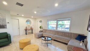 Una sala moderna con un sofá color beige, otomanas amarillas, una mesa de centro y un sillón verde.