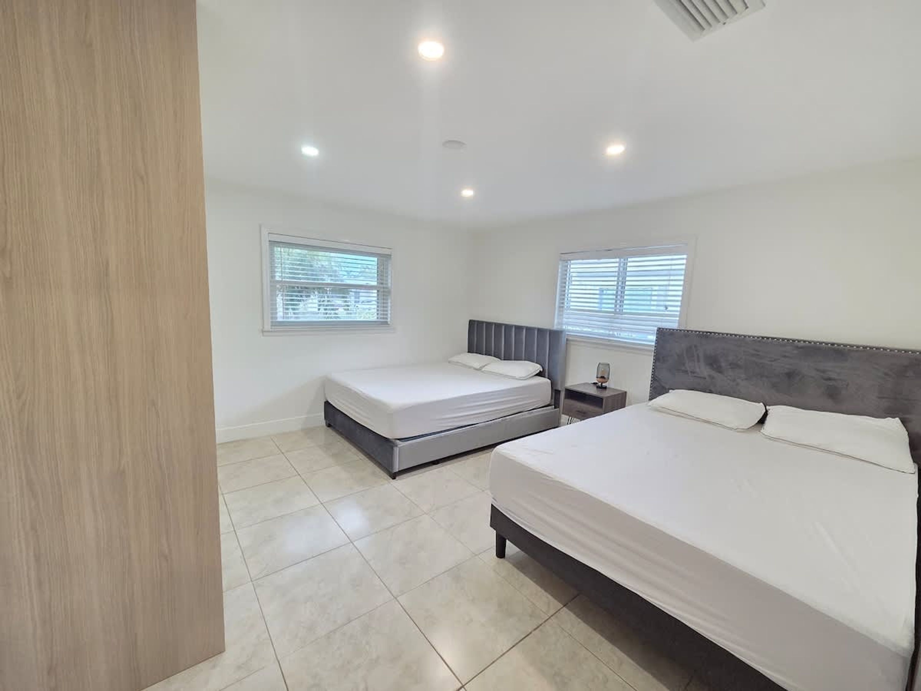 A bedroom with two beds, a nightstand, and a window with blinds.
