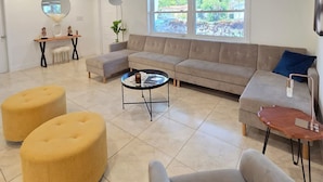 Amplio salón con un sofá color beige, una mesa redonda de centro y dos otomanas.