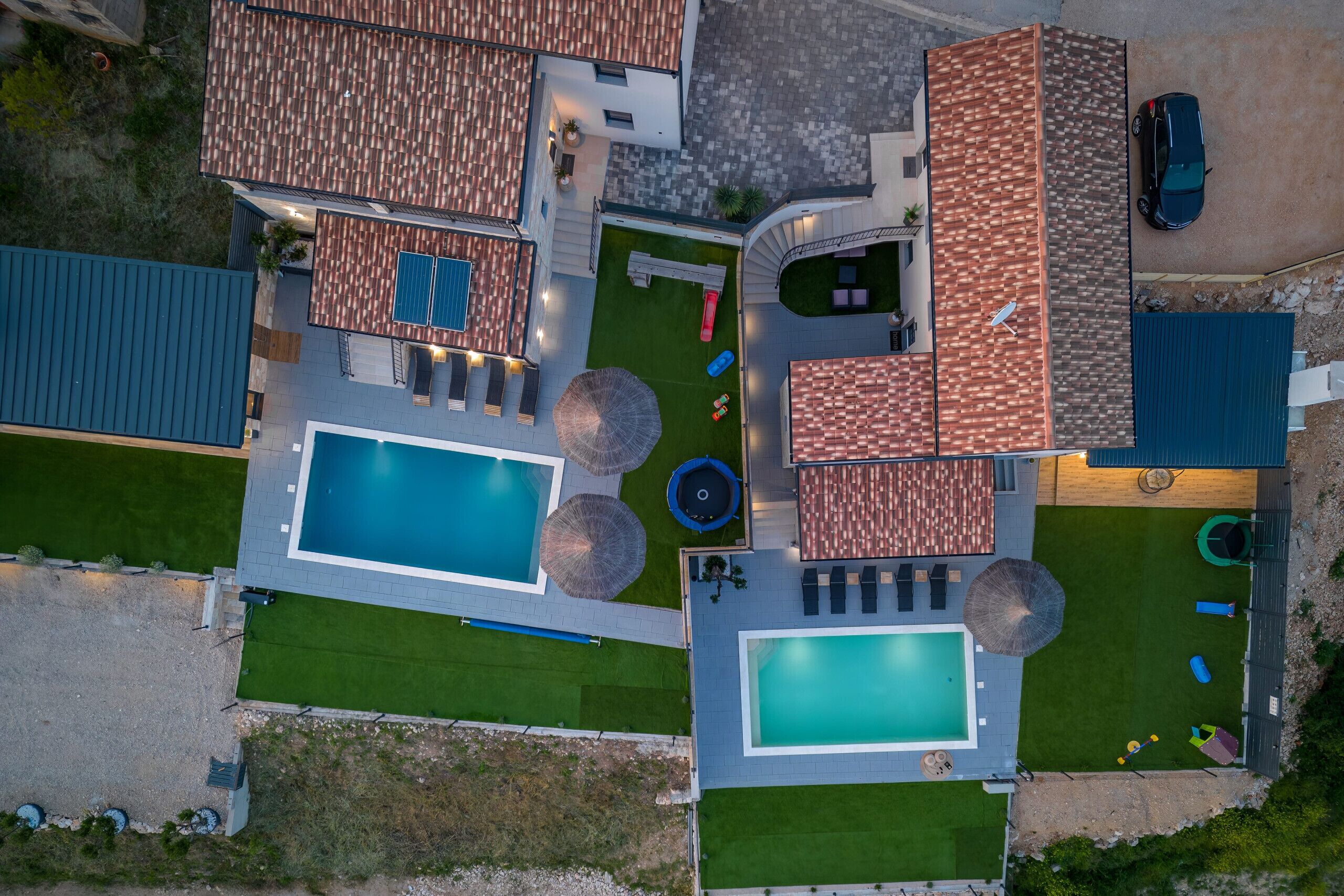 Vue aérienne d’une propriété résidentielle dotée de deux piscines, d’un patio couvert et d’une voiture garée à l’extérieur.