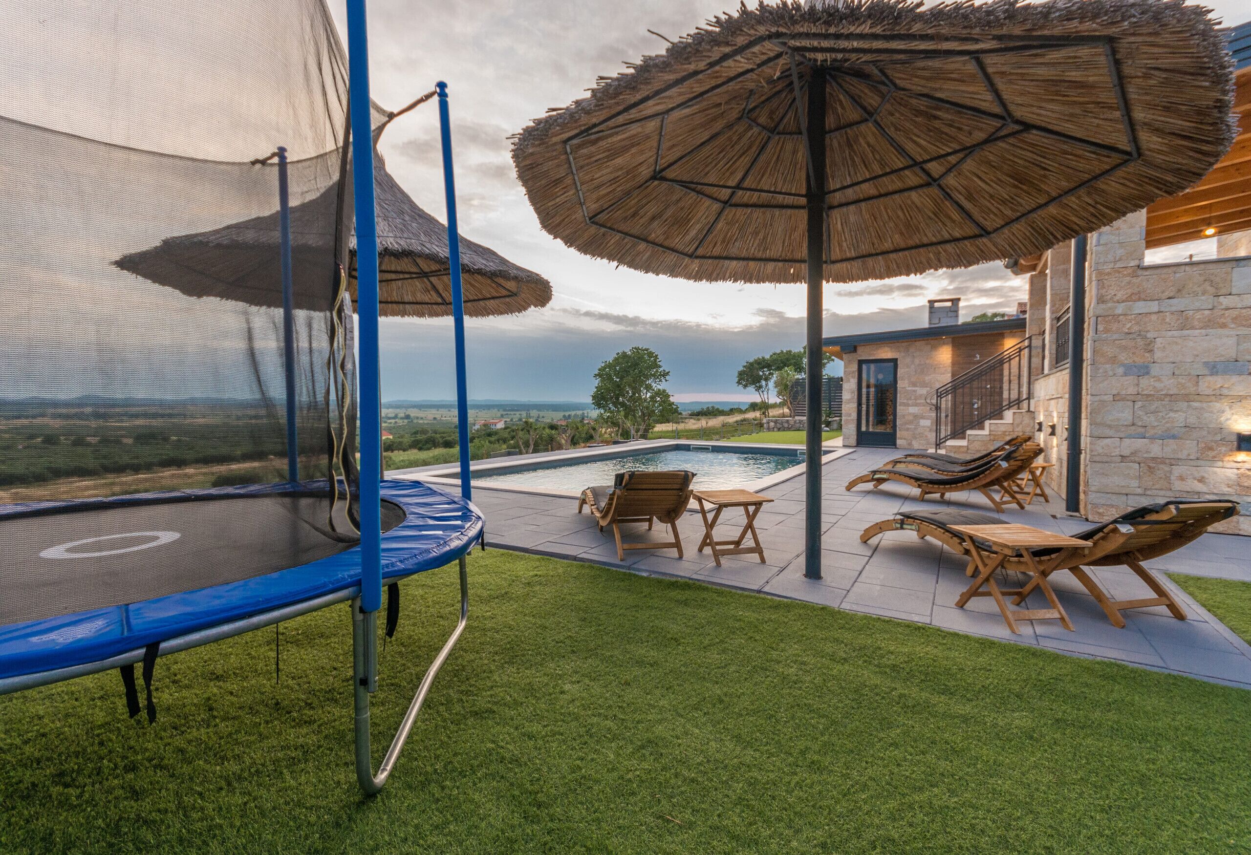 A backyard with a trampoline, outdoor seating, a pool, and a view of the landscape.