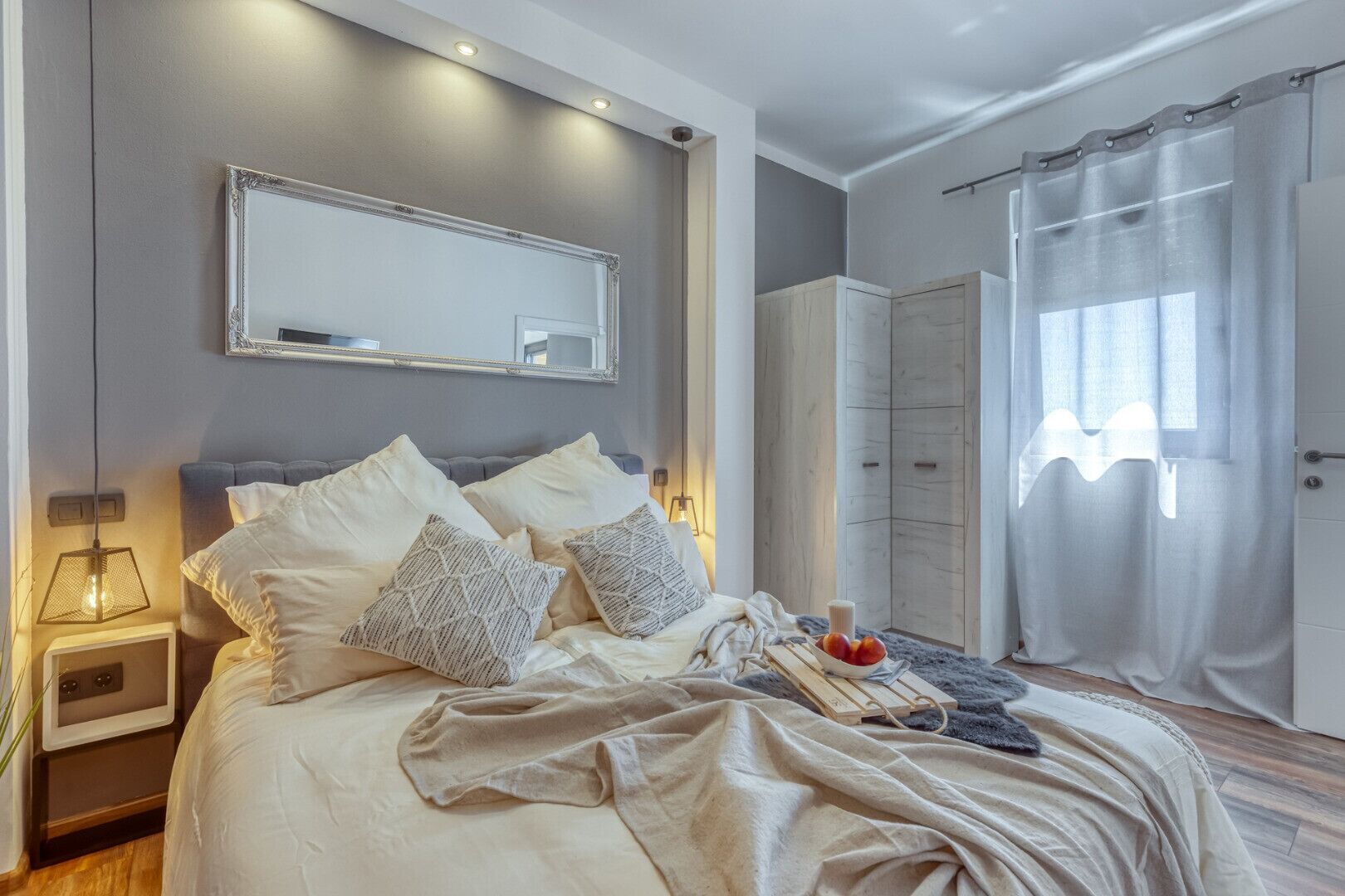Ett modernt sovrum med en stor säng, sänglampor, en spegel och en garderob.