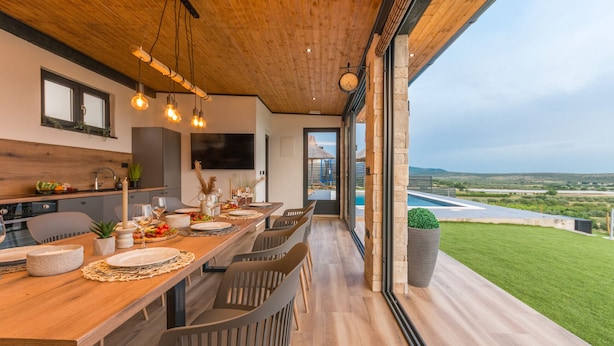 A modern dining area with a wooden ceiling and large windows overlooking a pool and landscape. - Villa La Vrana Zadarvillas (Pakostane)