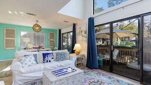 A spacious living area with a white sofa, patterned rug, and a large window with a view of the outdoors. - 7 Ocean Gate Villas: 2 Bedroom South Forest Beach Villa (Hilton Head Island)