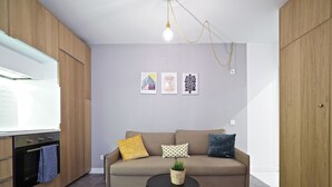 A compact living space with a kitchenette, a sofa with patterned cushions, a small round table with a plant, and hexagonal patterned flooring. - Torrassa Cozy Apartment by Olala Homes (L'Hospitalet de Llobregat)