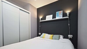 A bedroom with a bed, a nightstand, a wall-mounted shelf with two framed pictures, and a sliding door closet. - Torrassa Cozy Apartment by Olala Homes (L'Hospitalet de Llobregat)