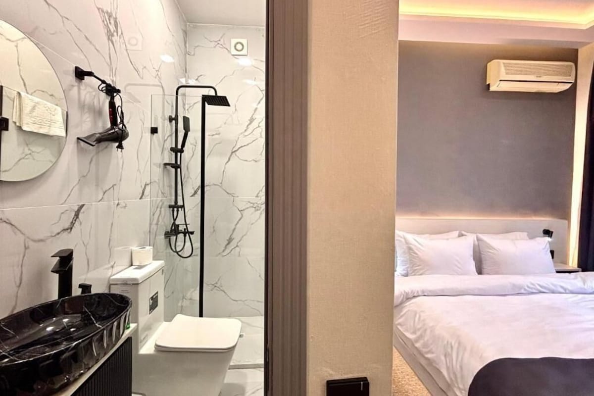 Un baño moderno con pared de mármol, una bañera negra y un inodoro.